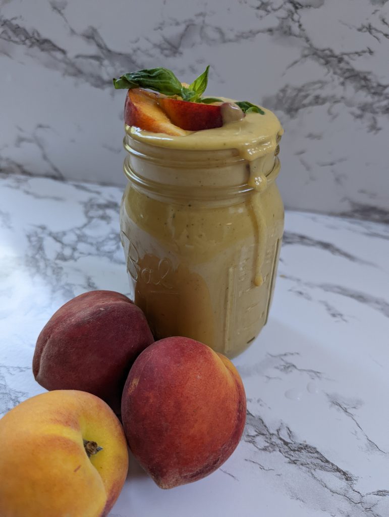 A jar overflowing with peach basil smoothie and extra peaches next to the glass