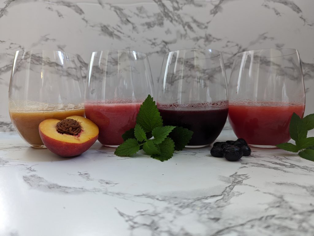 4 glassing holding different colored margaritas with garnishes in front of the glasses