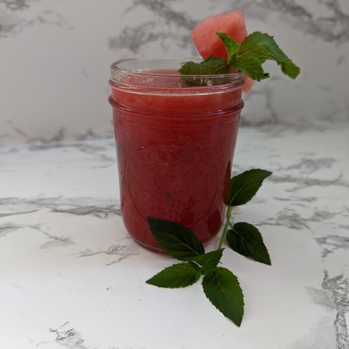 A mason jar filled with a pink watermelon margarita topped with a piece of watermelon and a sprig of mint