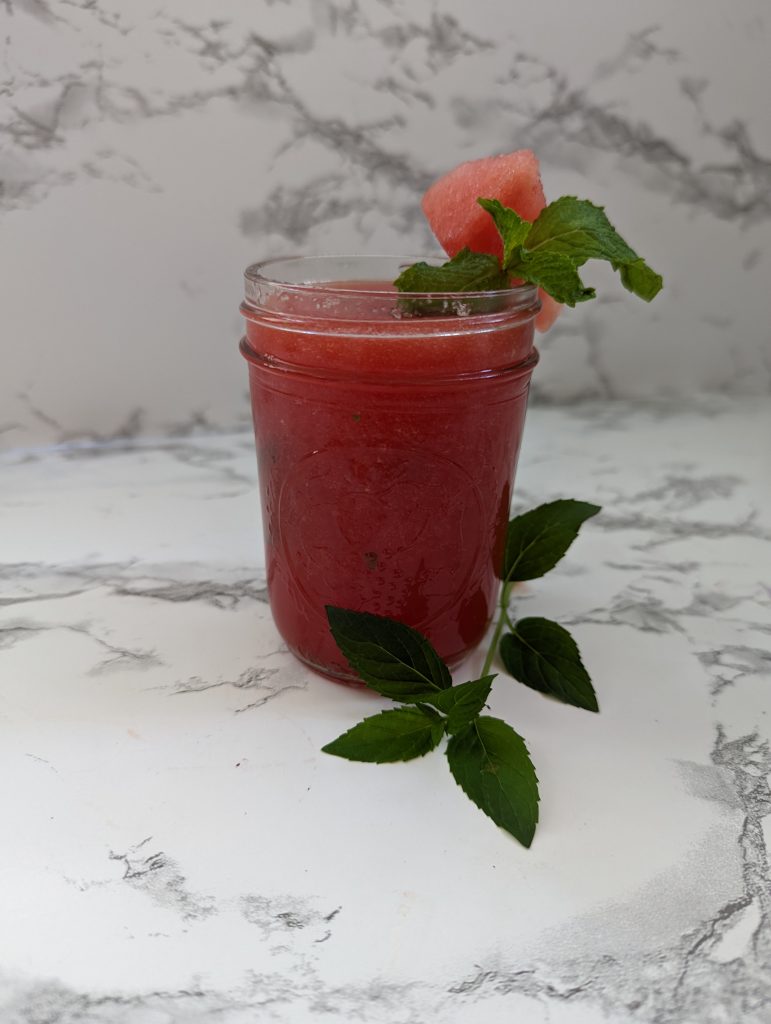 A mason jar filled with a pink watermelon margarita topped with a piece of watermelon and a sprig of mint