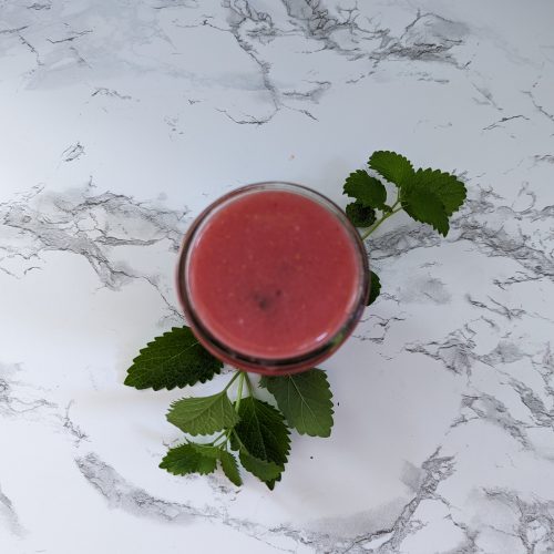 A raspberry margarita with lemon balm around the glass.