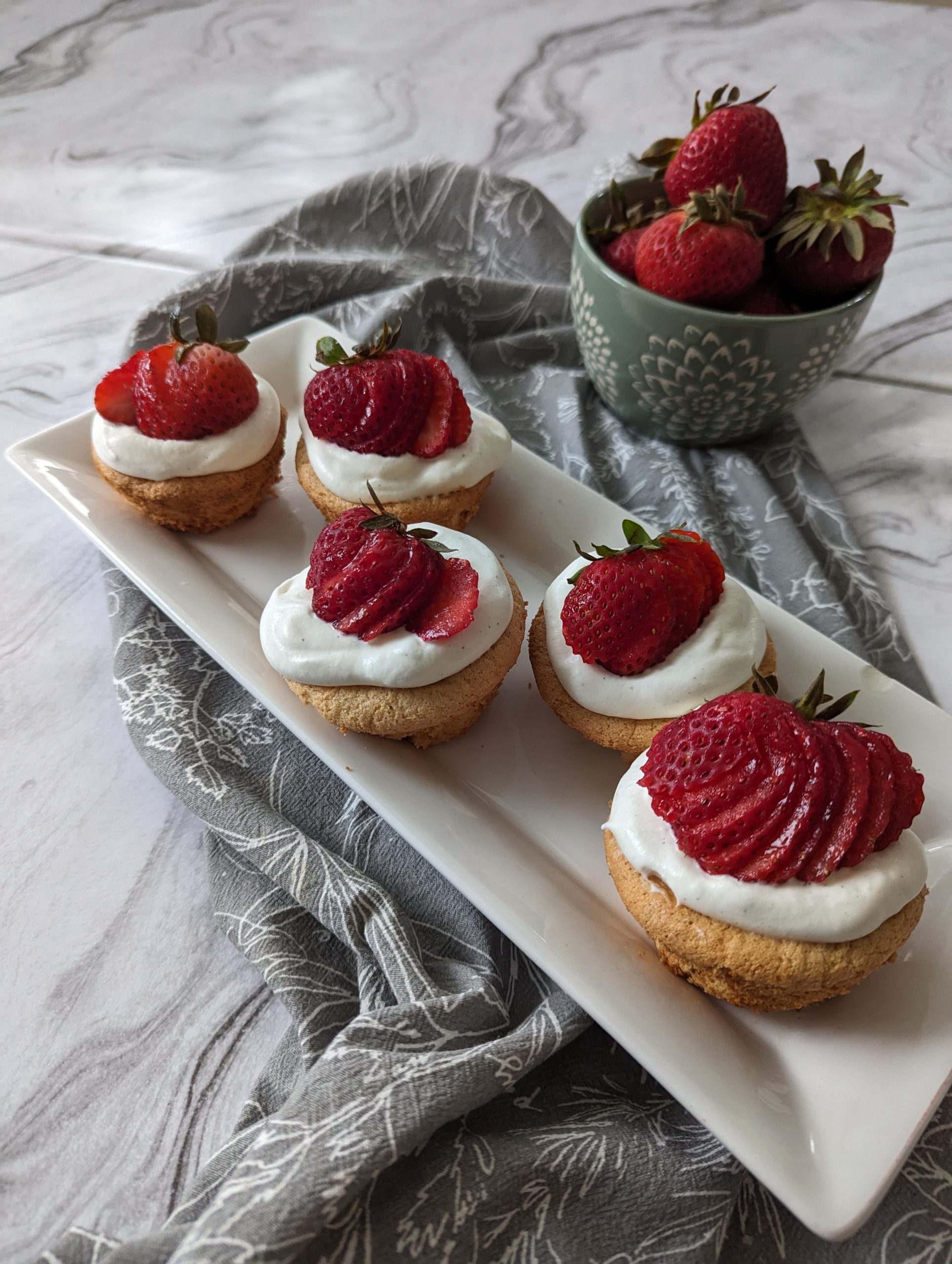 a plate of strawberry shortcake cups topped with whipped cream and a strawberry cut into a fan