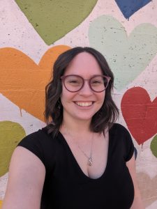 Colie, a white girls with medium length brown hair smiling in front of a heart-covered wall